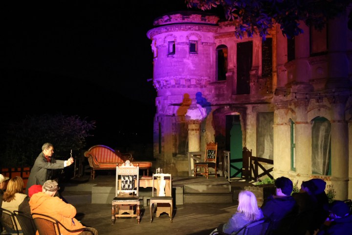 Outdoor night theater at castle ruins with audience.