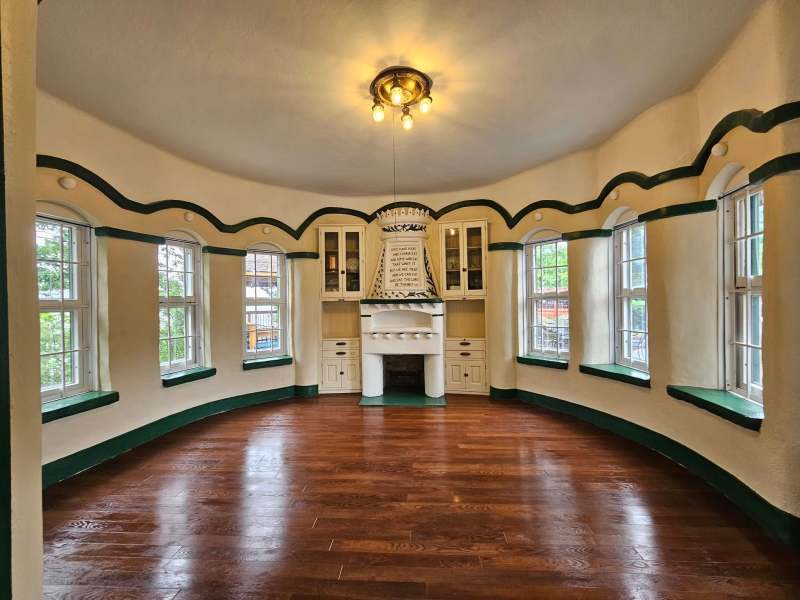 Round room with wooden floor, central fireplace, and arched windows.