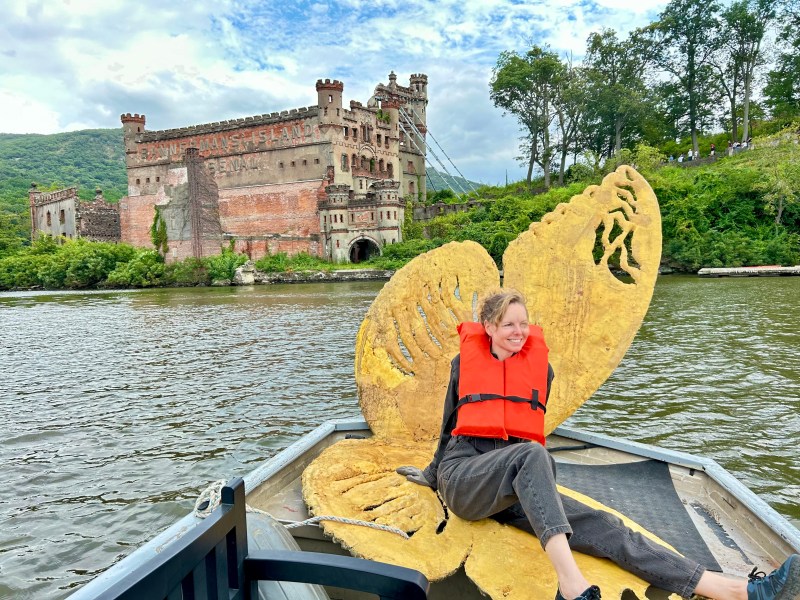 Person in orange life vest sitting on a boat with butterfly wings sculpture, castle in the background.